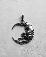 Silver moon face pendant with detailed carving and an oxidized finish, shown flat on a light grey textured surface.