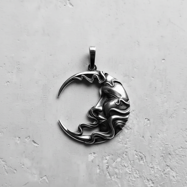 Silver moon pendant with an artistic human face and flowing hair design, shown flat on a textured white surface.