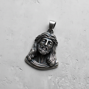 Oxidized silver Jesus pendant showing detailed crown of thorns and flowing hair, displayed on a light gray textured surface.