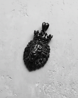 Black rhodium plated sterling silver lion pendant with crown, angled to show the dark, matte finish on a grey texture.