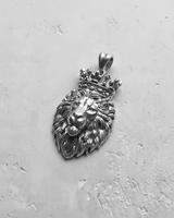Silver lion pendant with an ornate crown, showing detailed mane texture and regal facial expression on a gray background.