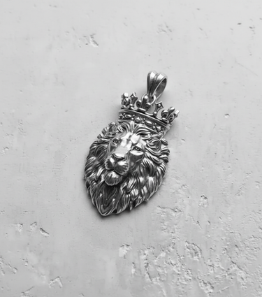Silver lion pendant with an ornate crown, showing detailed mane texture and regal facial expression on a gray background.