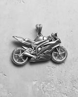 Silver motorcycle pendant showing detailed side profile, engine, and aerodynamic fairings, resting on a textured gray background.