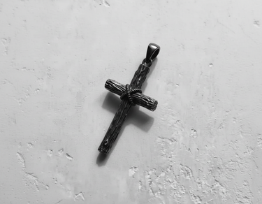 Oxidized Silver Rustic Cross Pendant with a detailed wood grain texture and tightly wound rope center on a textured surface.
