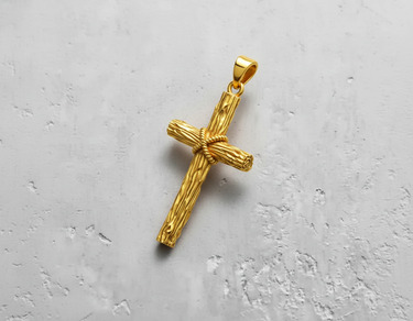 Gold vermeil rustic cross pendant featuring a detailed wood-grain texture and rope-wrapped center, angled on a white textured surface.