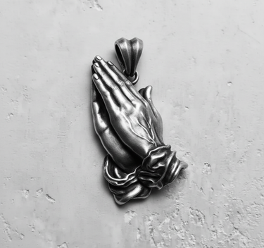 Angled side view of the silver praying hands pendant, showcasing the three-dimensional craftsmanship of the clasped hands and cuffs.
