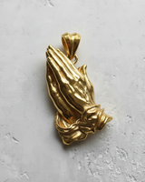 14K Gold Vermeil praying hands pendant showing detailed, clasped fingers and elegant cuffs on a light textured surface.