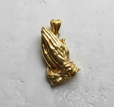 14K Gold Vermeil praying hands pendant showing detailed, clasped fingers and elegant cuffs on a light textured surface.