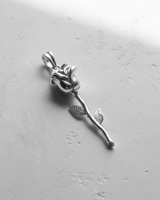Polished 925 sterling silver rose pendant with a detailed bloom and long stem, shown angled on a white textured surface.
