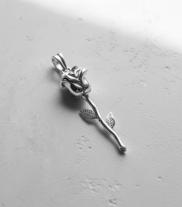 Polished 925 sterling silver rose pendant with a detailed bloom and long stem, shown angled on a white textured surface.