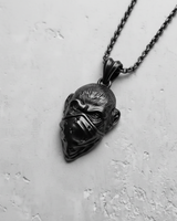 Black rhodium-plated silver monkey pendant with bandana on a matching dark chain, shown against a light concrete surface.
