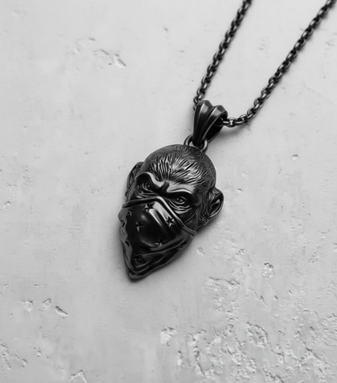 Black rhodium-plated silver monkey pendant with bandana on a matching dark chain, shown against a light concrete surface.