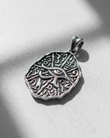 Angled view of oxidized silver Egyptian pendant showing irregular ancient coin shape and textured surface