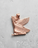 Rose gold plated silver Isis pendant showing the kneeling goddess with outstretched wings, detailed on a textured grey surface.