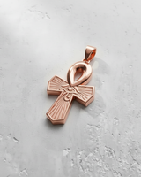 Egyptian Ankh pendant in a polished rose gold finish, featuring the Eye of Horus on a light grey textured surface.