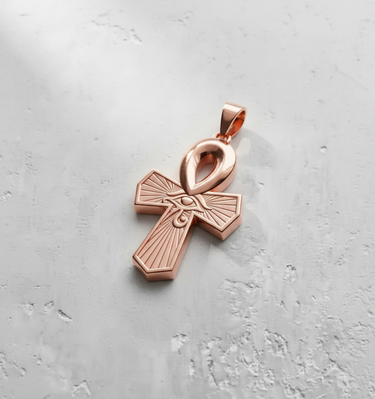 Egyptian Ankh pendant in a polished rose gold finish, featuring the Eye of Horus on a light grey textured surface.