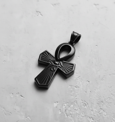 Black rhodium plated silver Ankh pendant with a detailed Eye of Horus and radiating lines, on a textured light gray surface.