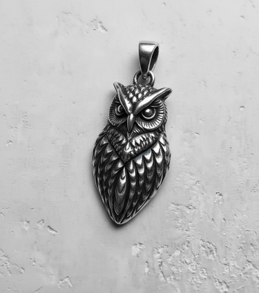 Oxidized silver owl pendant with intricate feather and facial details, shown from the front on a textured light gray surface.