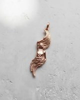 Rose gold plated angel wing pendant with a polished female figure and detailed feathers, shown on a textured white surface.
