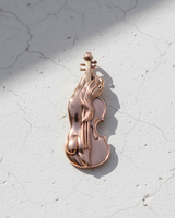 Rose gold-plated silver violin pendant with flowing hair details, casting a soft shadow on a cracked white concrete surface.