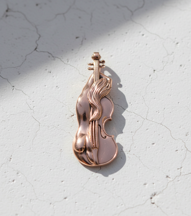 Rose gold-plated silver violin pendant with flowing hair details, casting a soft shadow on a cracked white concrete surface.