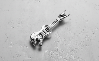 Polished silver skull guitar pendant with a rock hand gesture headstock, shown from a top-down angle on a gray surface.