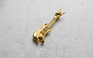 Gold vermeil rock guitar pendant featuring a skull body and 'rock on' hand gesture, shown on a textured light gray surface.