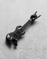 Black rhodium plated silver rock guitar pendant with a skull body, shown at an angle on a textured grey surface.