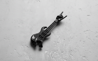 Black rhodium plated silver rock guitar pendant with a skull body, shown at an angle on a textured grey surface.