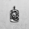 Silver ornate skull pendant with an oxidized finish, showcasing the high-relief swirling design on a concrete background.
