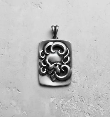 Silver ornate skull pendant with an oxidized finish, showcasing the high-relief swirling design on a concrete background.