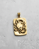 Gold vermeil ornate silver skull pendant with a high-relief baroque swirl design, shown on a light grey textured surface.