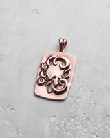 Rose gold ornate skull pendant featuring a side-profile skull and swirling patterns, shot from a top-down angle.