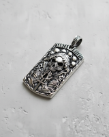 Angled view of rectangular silver dog tag pendant featuring high relief skull figure and gothic text inscription