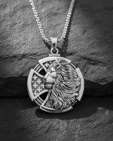 Silver lion cross pendant with chain, showing the detailed lion head and interwoven cross design on a dark slate background.