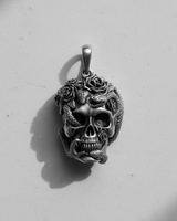 Silver skull snake pendant with rose details in a dramatic black and white photo showing deep oxidized shadows.