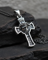 Silver Jesus Cross Pendant with an oxidized finish and chain, shown at an angle on pieces of dark, textured slate rock.