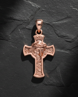 Rose gold plated Jesus cross pendant with detailed face and crown of thorns, shot from above on a dark slate background.