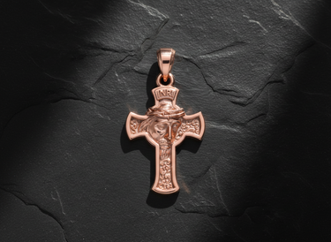 Rose gold plated Jesus cross pendant with detailed face and crown of thorns, shot from above on a dark slate background.