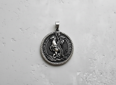 Silver Saint George pendant with detailed high relief of the knight and dragon on a textured light grey surface.