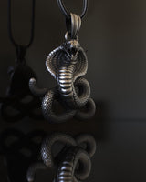 Side angle view of handcrafted cobra pendant showing coiled serpent body and oxidized finish details