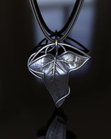 Handcrafted 925 sterling silver leaf pendant showing polished highlights and oxidized details on a black reflective surface.