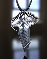Elven-style silver leaf pendant with detailed veins, suspended from a braided chain against a soft-focus background.