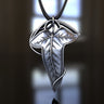 Elven-style silver leaf pendant with detailed veins, suspended from a braided chain against a soft-focus background.
