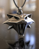 Angled view of the handcrafted Witcher Cat School pendant, highlighting the sharp ears and detailed fangs of the silver design.