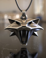 The 925 sterling silver Witcher Cat medallion hanging from a chain, showing its 3D depth and polished finish on a marble surface.