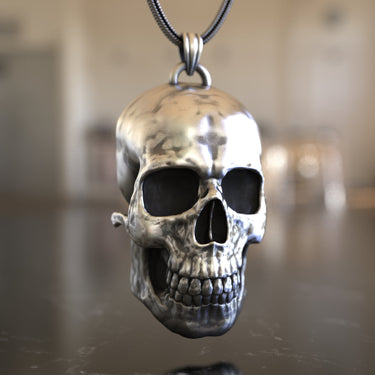 Three-quarter angle of the handcrafted silver skull pendant, highlighting its realistic anatomical structure and oxidized finish.