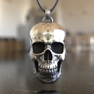 Front view of a 925 sterling silver skull pendant showing its polished, reflective surface hanging from a snake chain.