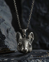 Oxidized 925 sterling silver mouse head pendant with detailed fur texture and large eyes, hanging on a chain against a dark rock.