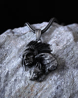 Oxidized sterling silver Native American pendant with chief, eagle, and wolf designs, resting on a textured gray rock.